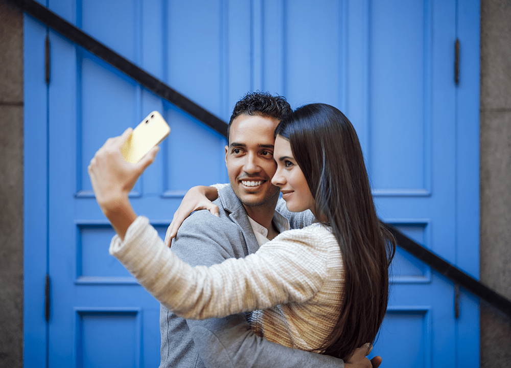 Pareja multiétnica se hace un selfie enfrente de su domicilio tras obtener el permiso de residencia
